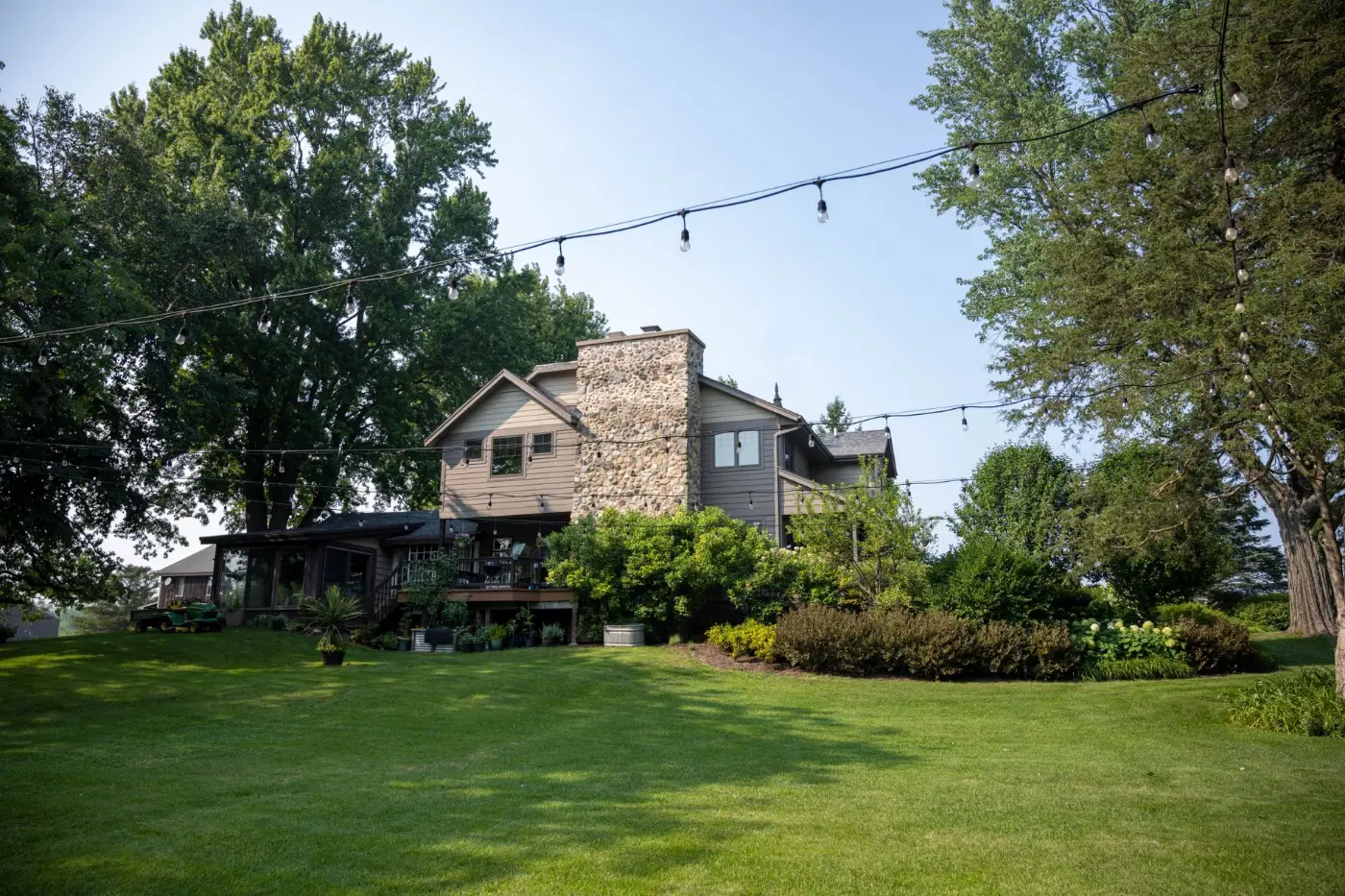 Residential home with a stone chimney, mature trees, and a lawn